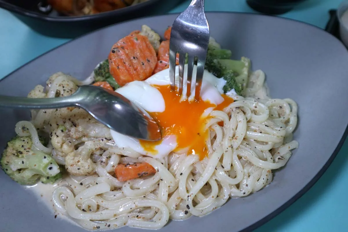 A poached egg breaking over Omu Place's cold truffle goma udon
